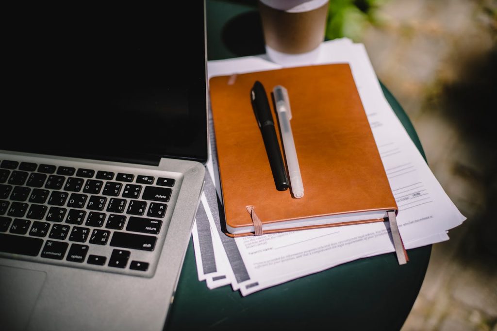 pexels-photo-4559555 Overhead view of a workspace with a laptop, notebook, and coffee cup on an outdoor table.