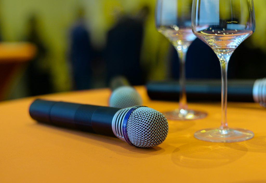 mic-microphone-sound-check-sing-722706-722706 Close-up of microphones and wine glasses on an orange table, ideal for events or entertainment themes.