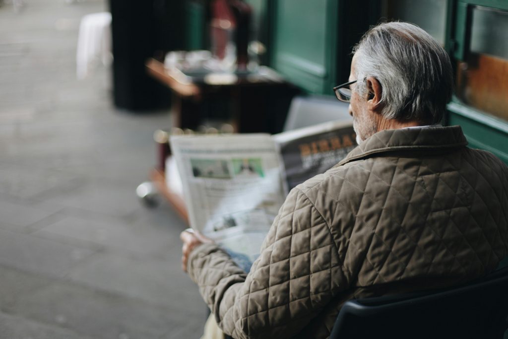 pexels-photo-1684916-1684916 Elderly man reading a newspaper in an outdoor cafe setting, enjoying a peaceful moment.