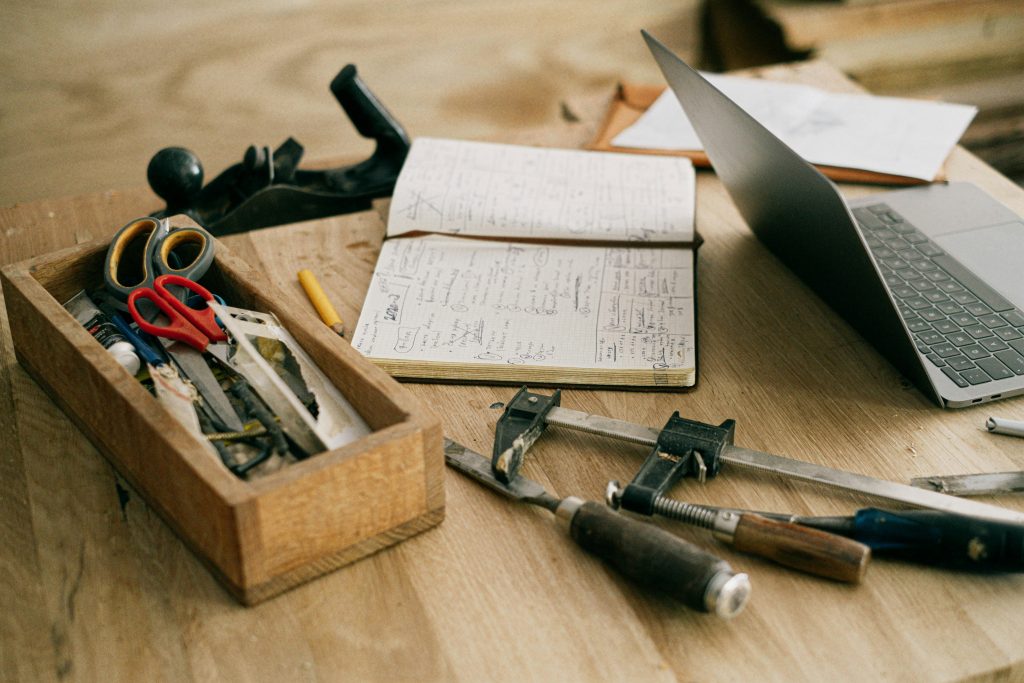 pexels-photo-4491908-4491908 A creative woodworking workspace with tools, notebook, and laptop on a wooden table.